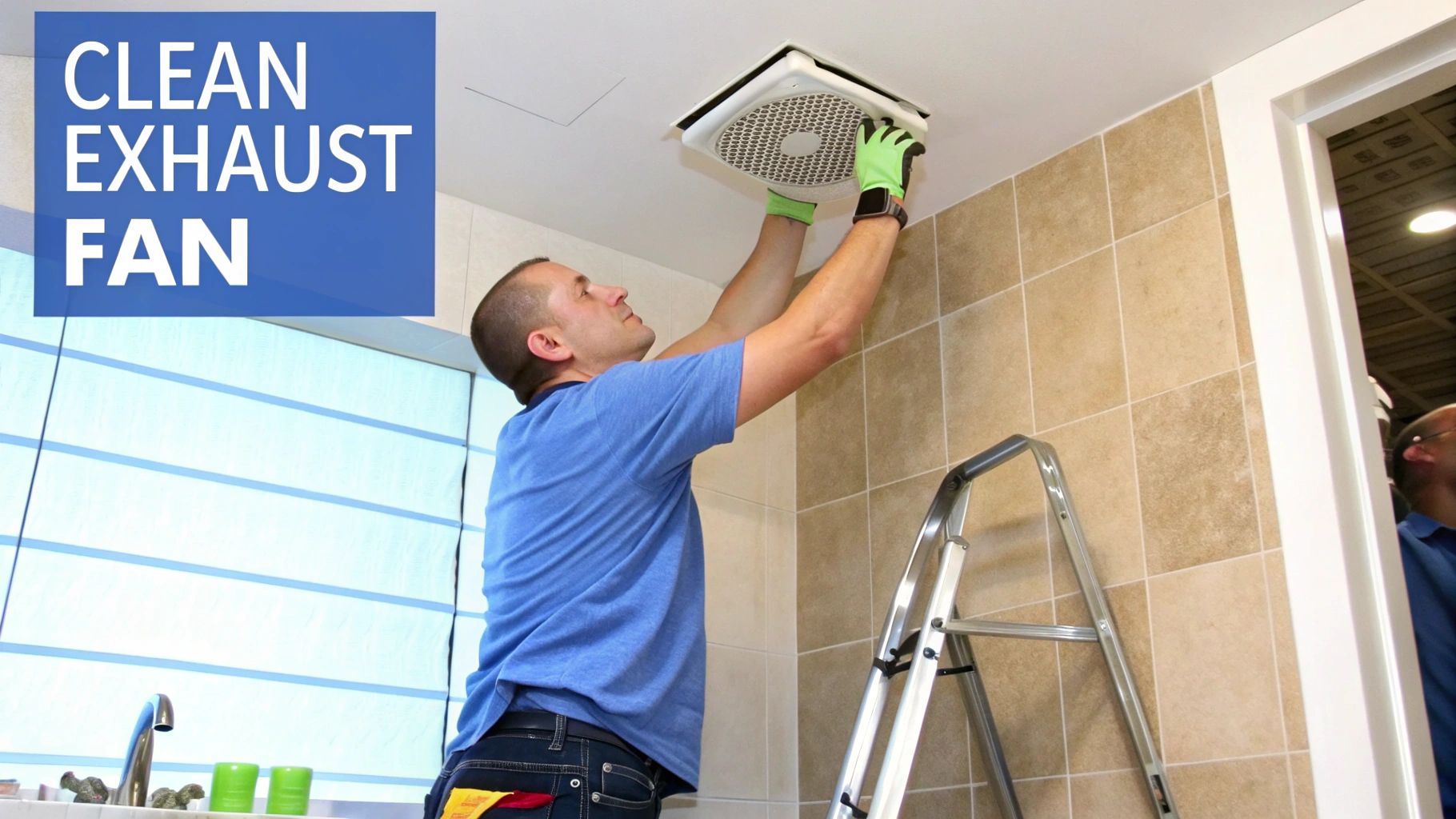 A man cleaning a bathroom ceiling exhaust fan. He is weraing a blue shirt and one wall has tan tile going up to the ceiling in front of the metal ladder the man is standing on.