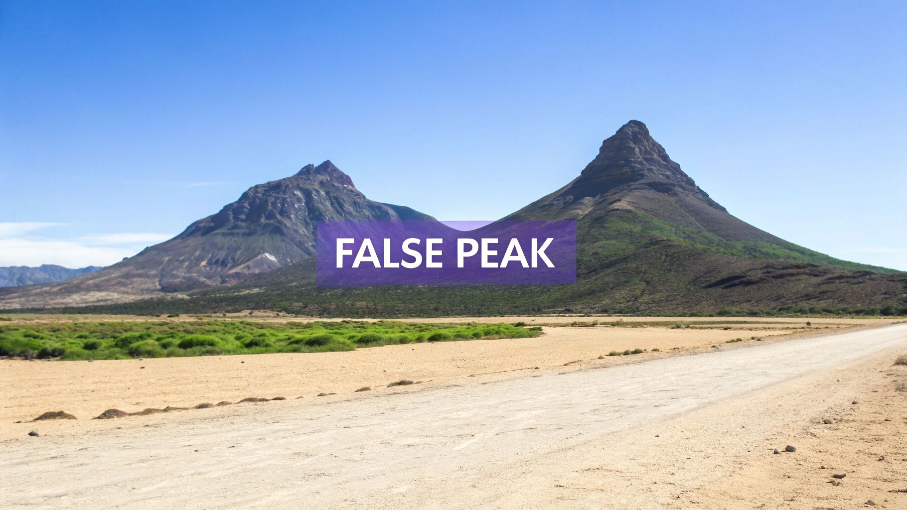 A wide scenic view of two large mountains and a dirt road in a desert landscape under a clear blue sky.