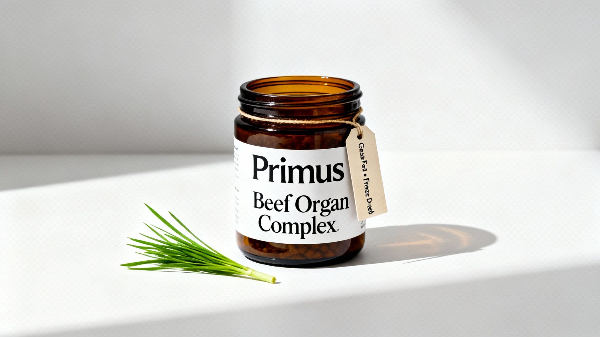 A brown glass jar of Primus Beef Organ Complex with a 'Grass Fed • Freeze Dried' tag, next to green chives on a white background.