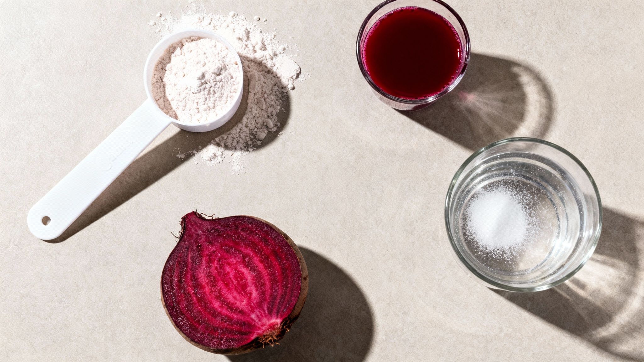 Ingredients for athletic performance: a cut beet, beet juice, protein powder in a scoop, and salt in water.