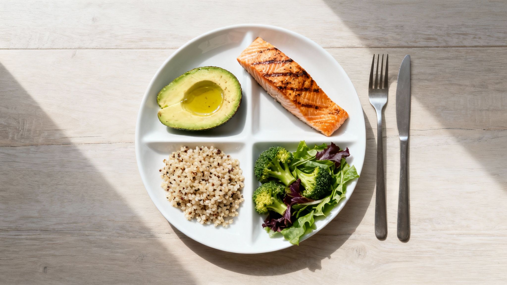 A healthy, balanced meal featuring grilled salmon, avocado, quinoa, and a fresh green salad on a partitioned plate.
