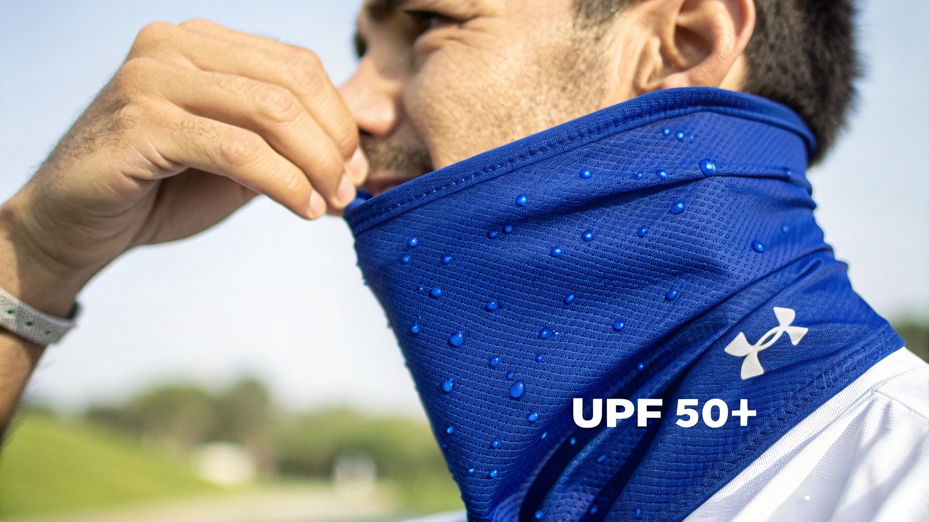 Close-up of a man wearing a blue Under Armour neck gaiter with water droplets, highlighting UPF 50+ sun protection.
