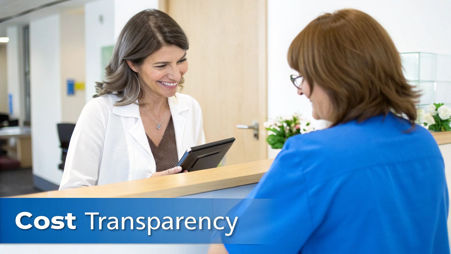 Two smiling women at a reception desk, one holding a tablet, discussing information.