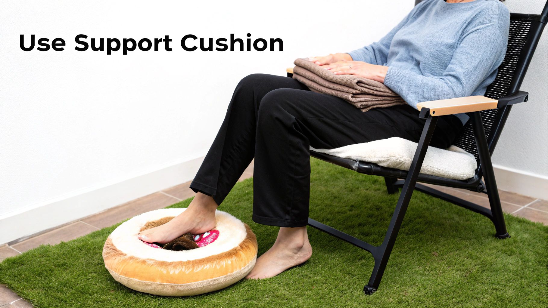 A person relaxing in a chair, with their bare feet resting comfortably on a round support cushion on artificial grass.