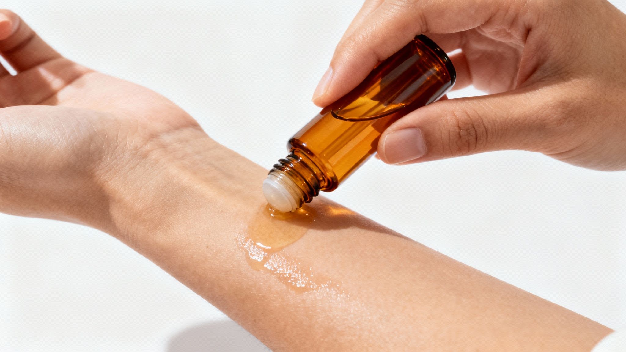 Close-up of a hand applying essential oil from an amber roll-on bottle onto a wrist.