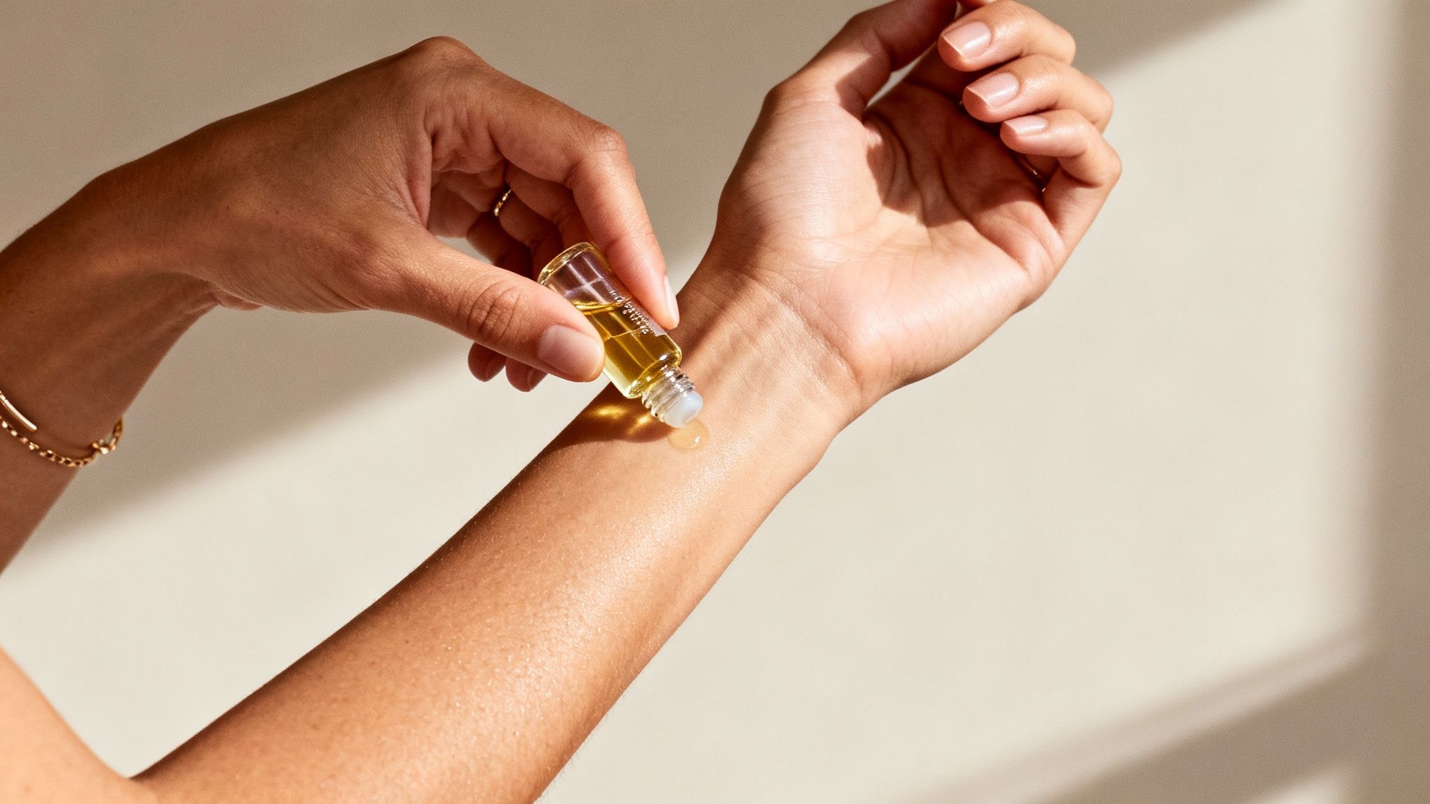A person's hands applying a golden roll-on oil to their wrist, highlighting skincare.