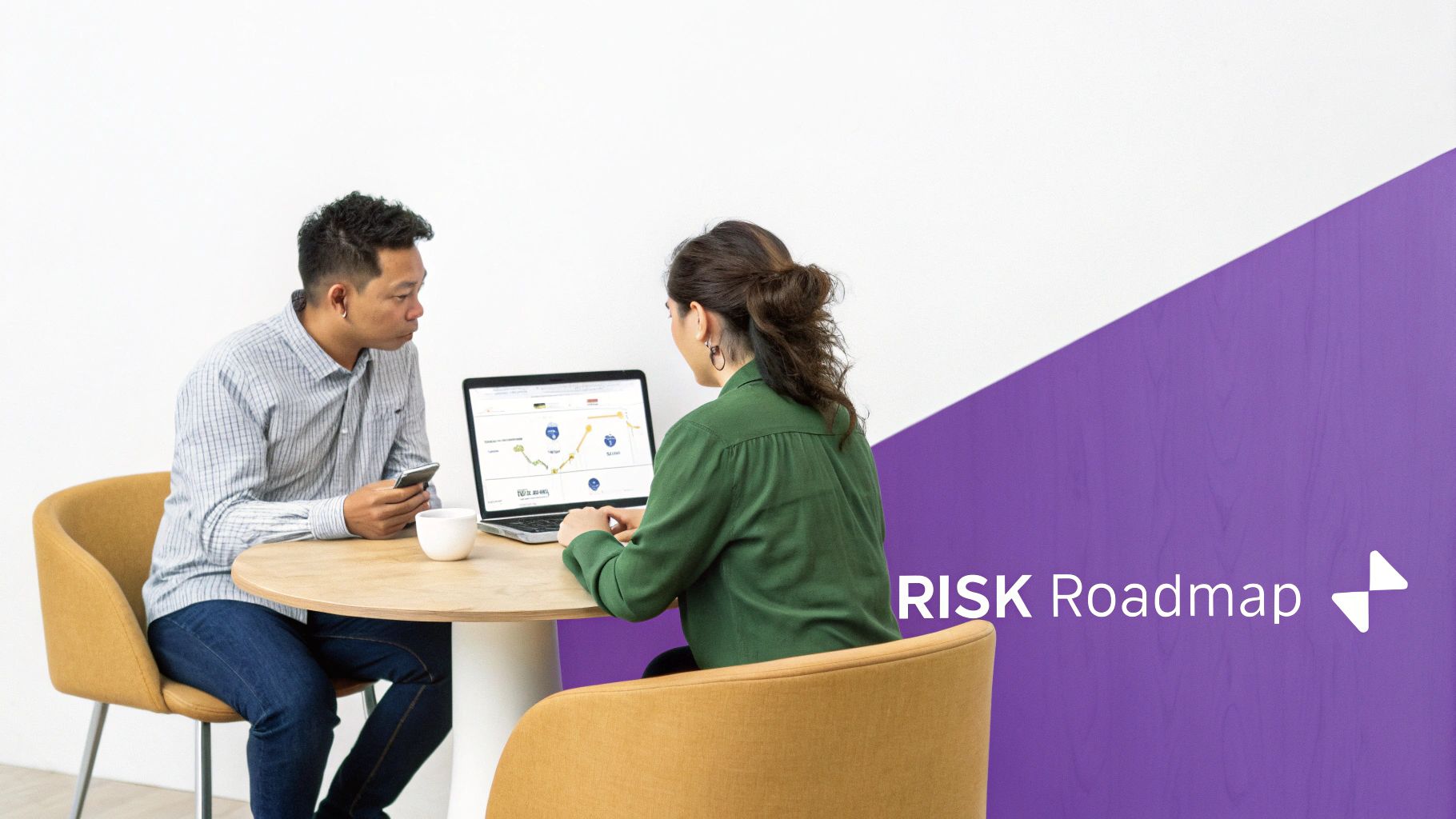 Two colleagues collaborate at a table, one using a laptop with charts, the other a phone.