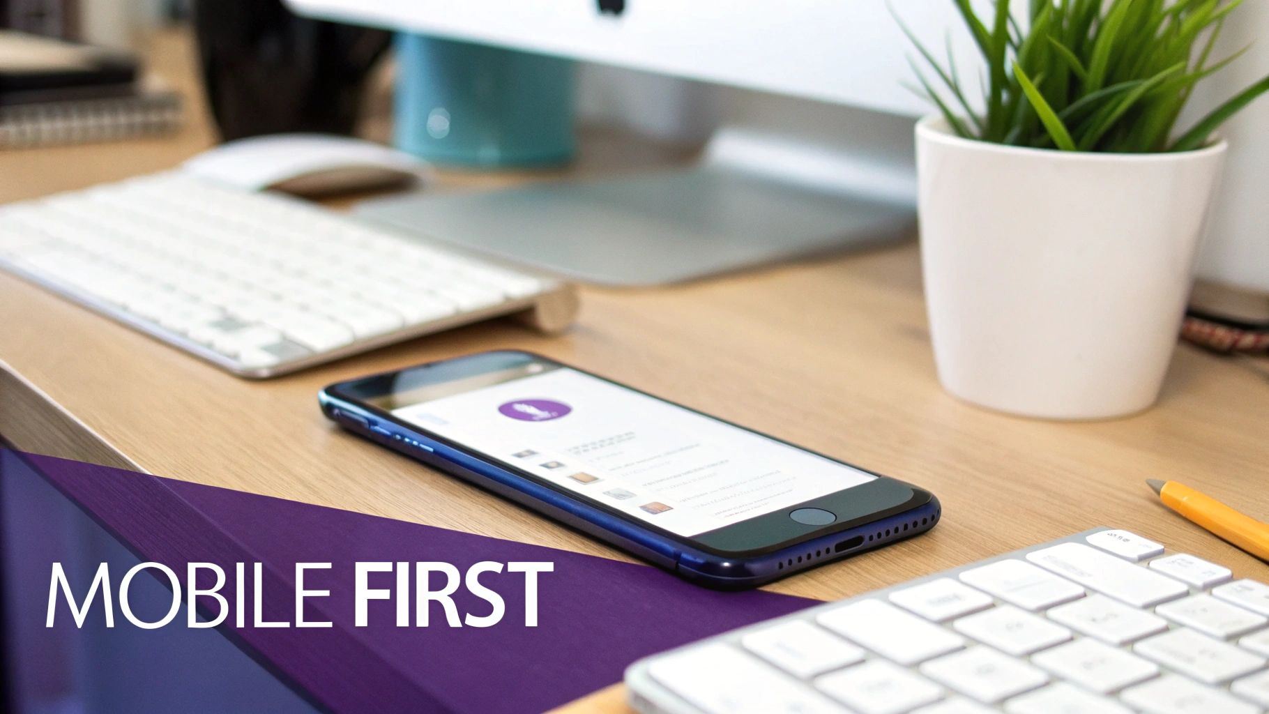 A smartphone displaying an app lies on a wooden desk next to a computer keyboard, with 'MOBILE FIRST' text.