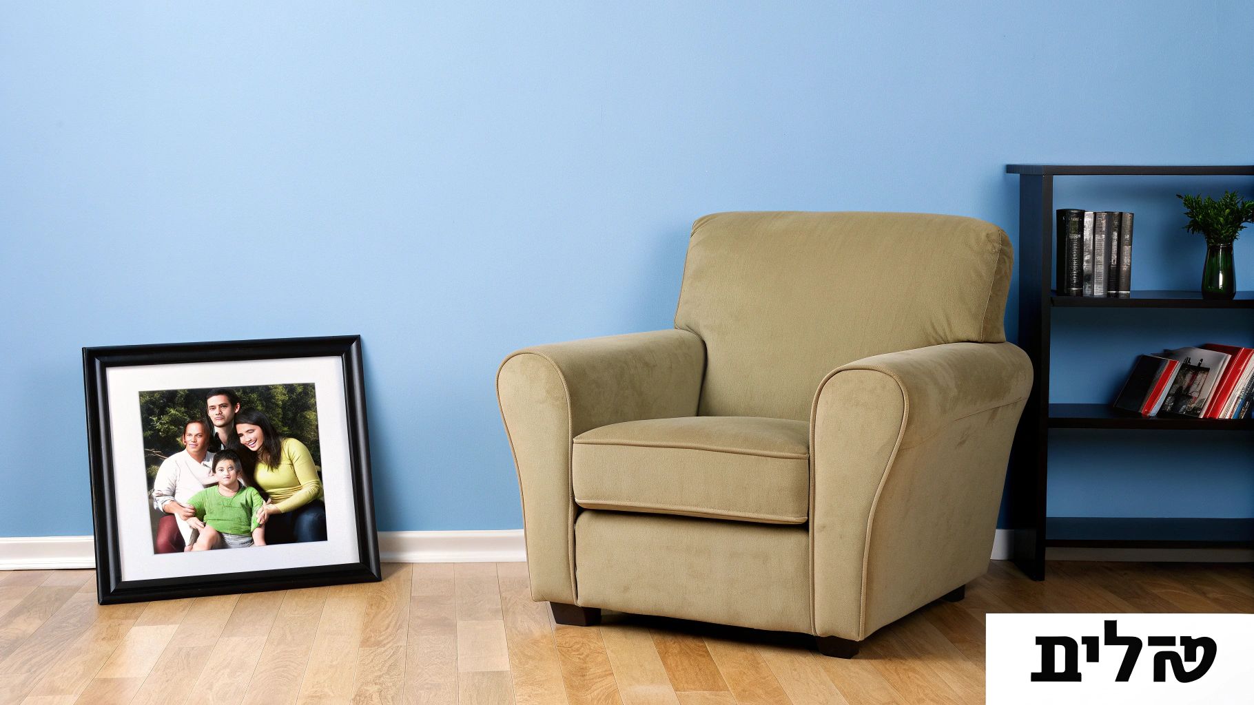 תמונה של כורסה נוחה על רקע קיר תכלת, לידה מדף ספרים ותמונה משפחתית גדולה.