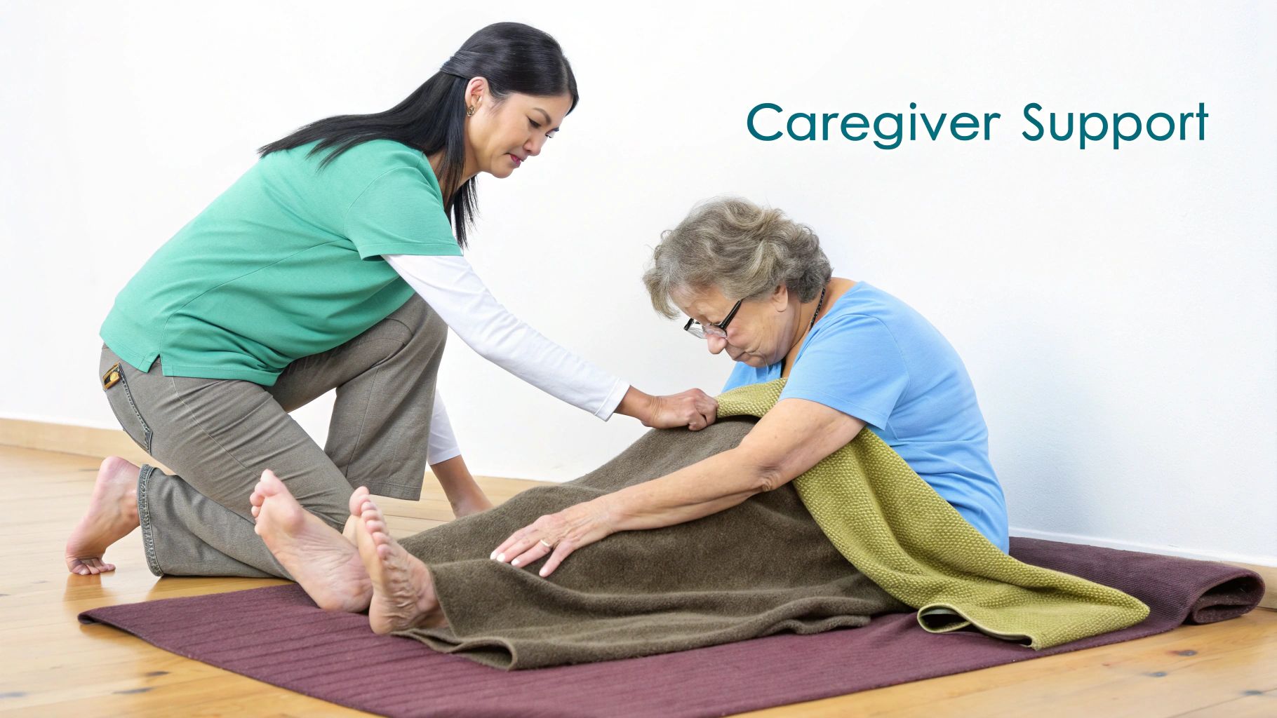 An Asian caregiver assists an elderly woman on the floor with blankets, offering support and comfort.