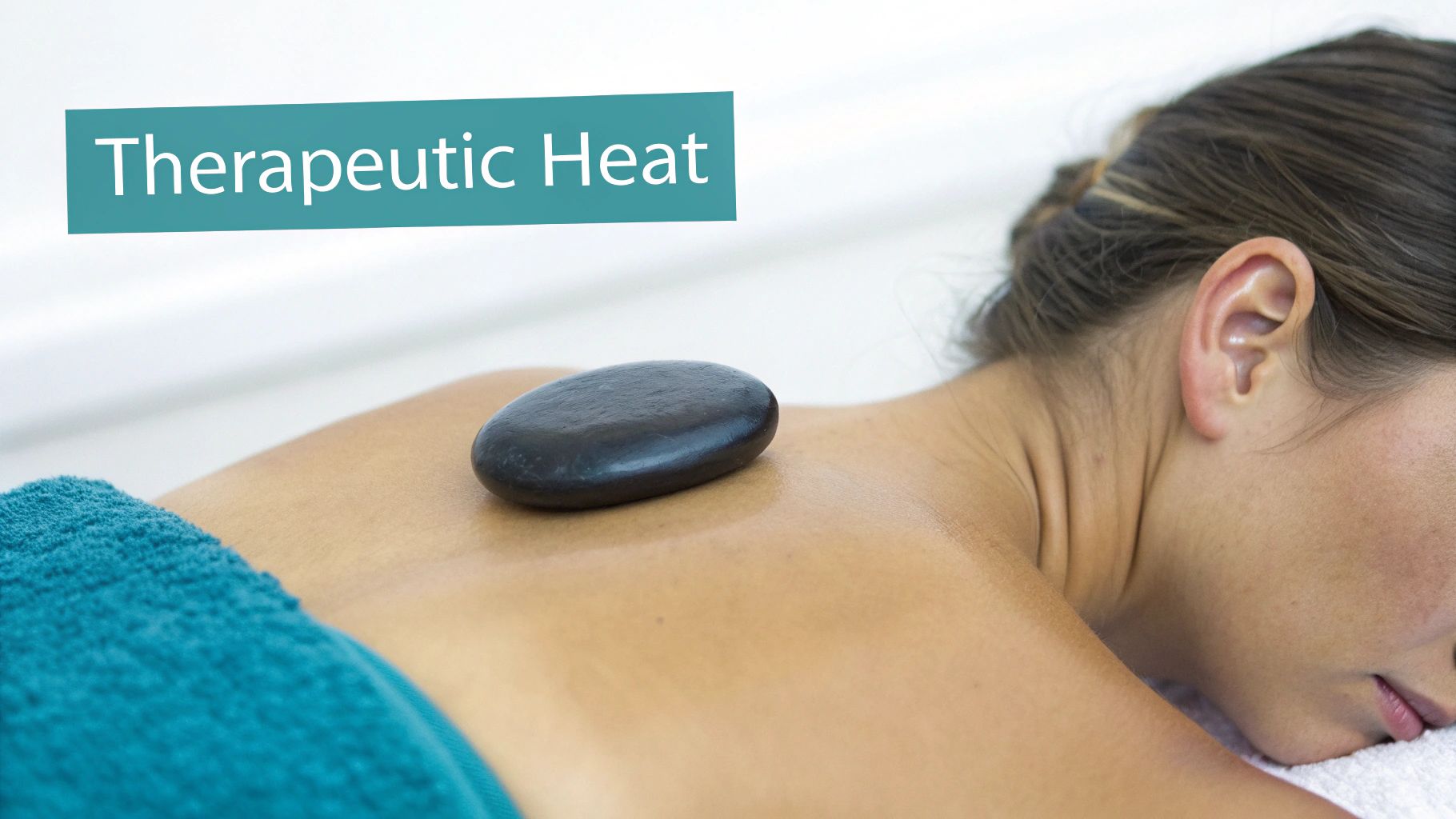 A person relaxing face down with a black hot stone on their back, emphasizing therapeutic heat.