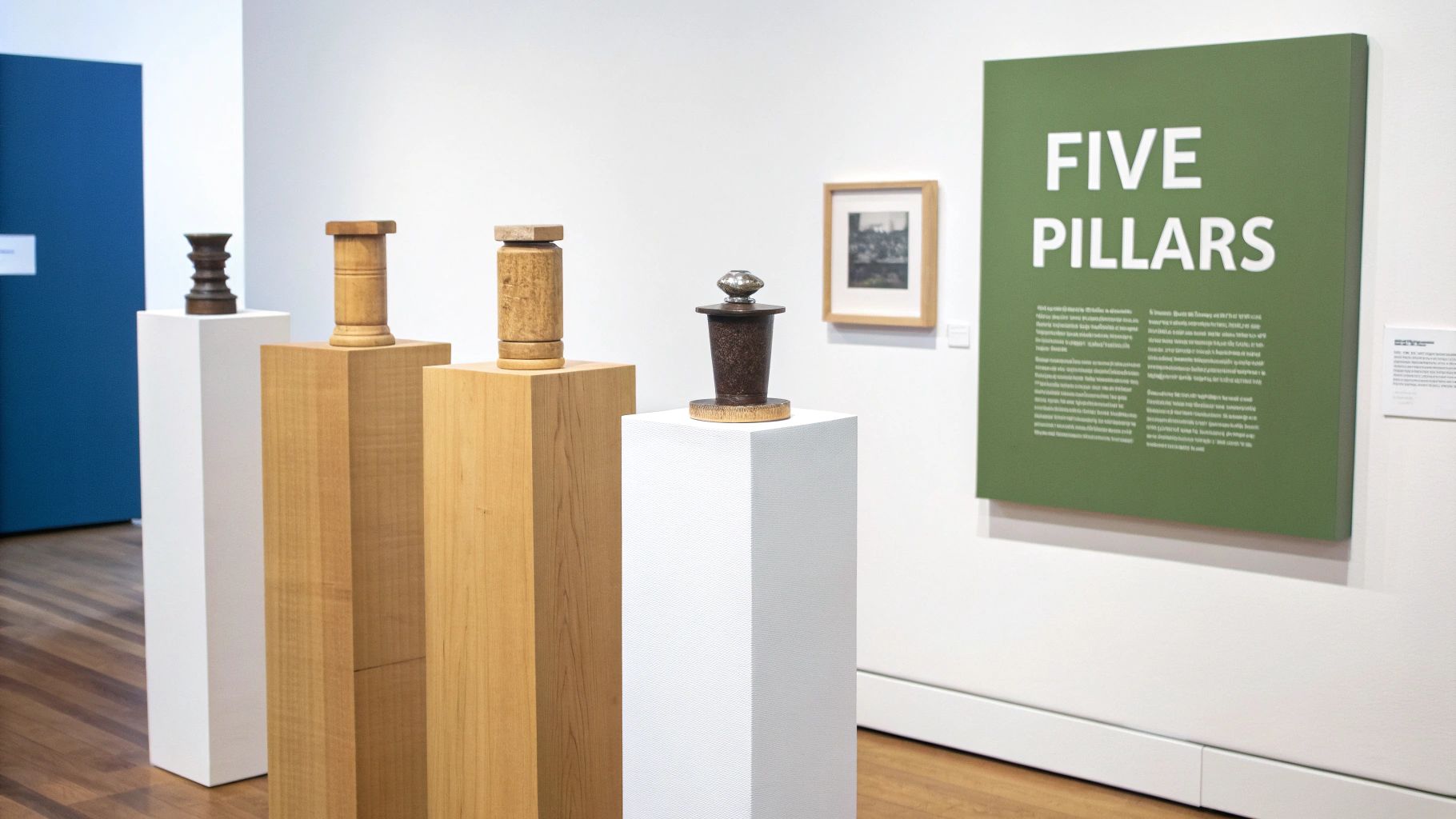 An art exhibition featuring unique wooden and metal sculptures on white and wood pedestals, with a green 'FIVE PILLARS' sign.