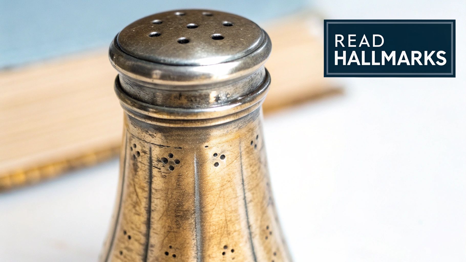 Close-up of an antique silver salt shaker with a perforated top, near a 'READ HALLMARKS' sign.