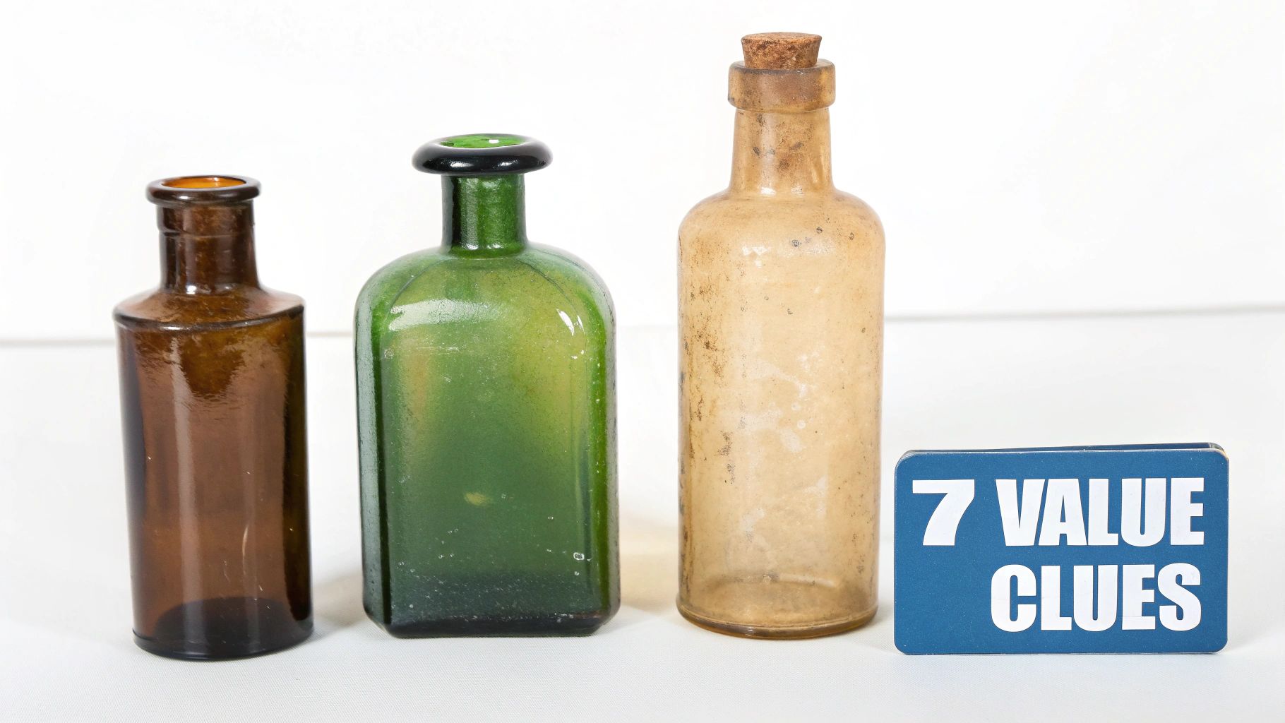 Three vintage glass bottles in brown, green, and clear with a cork, next to a '7 VALUE CLUES' sign.