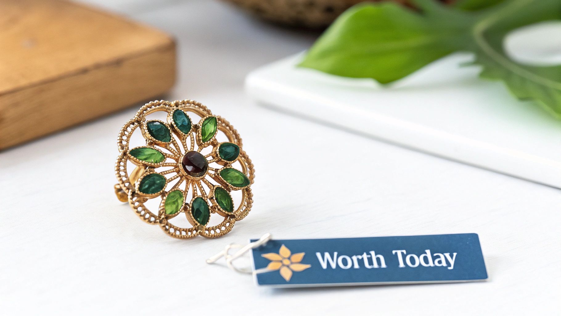 A beautiful gold filigree ring with green and dark red stones on a white surface, with a 'Worth Today' tag.
