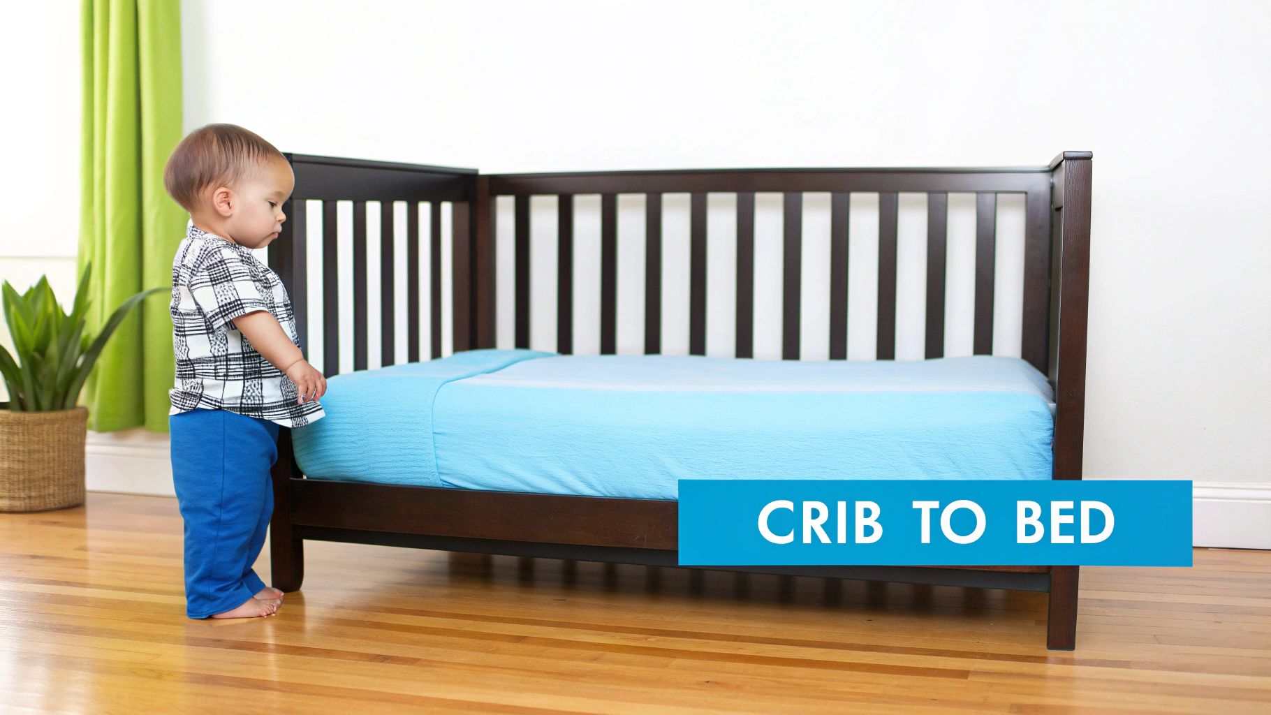 A toddler stands next to a dark wood crib converted into a bed with a blue sheet.