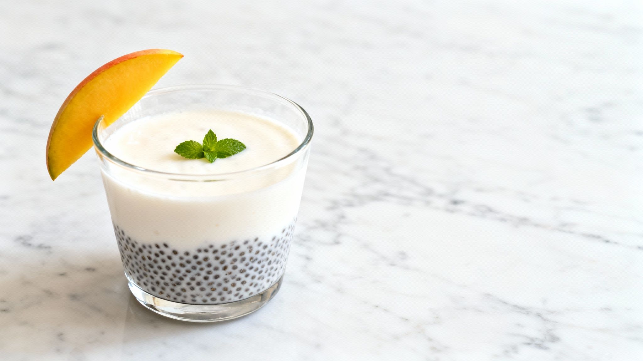 A refreshing basil seed pudding with a creamy yogurt layer, garnished with mango and mint on marble.