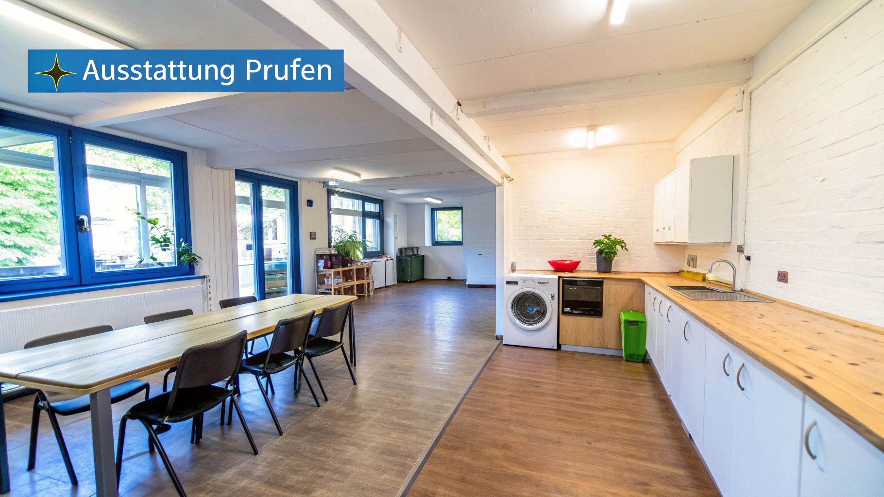 Geräumiger Gemeinschaftsraum mit langer Esstafel, moderner Küchenzeile und Waschmaschine in heller Umgebung.