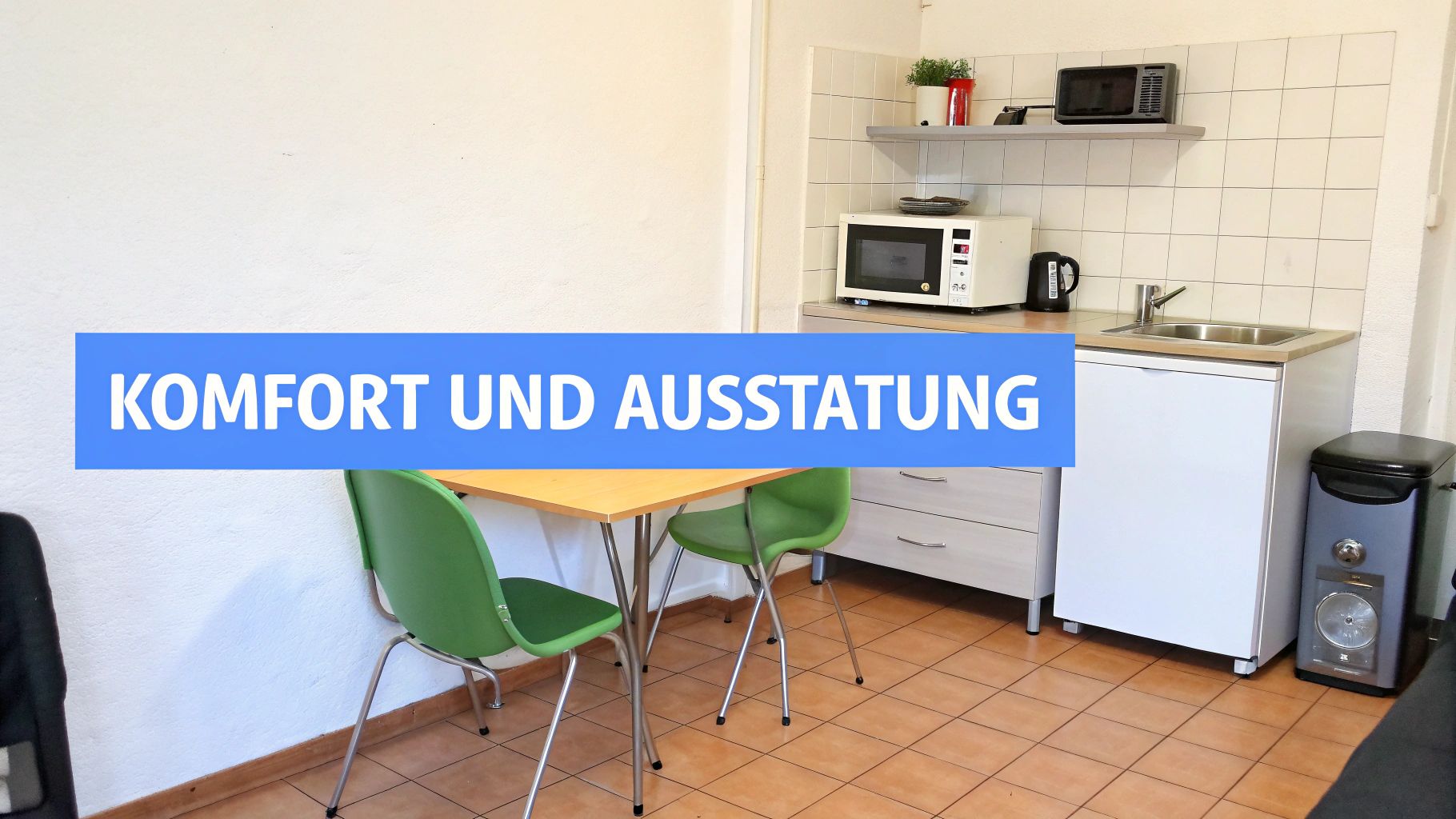 Eine funktionale Küchenzeile mit Mikrowelle, Spüle, Kühlschrank und Esstisch mit zwei Stühlen in einem Monteurzimmer.