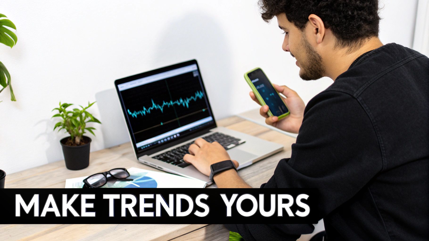 Young man analyzing financial data on a laptop and smartphone at a modern desk setup.
