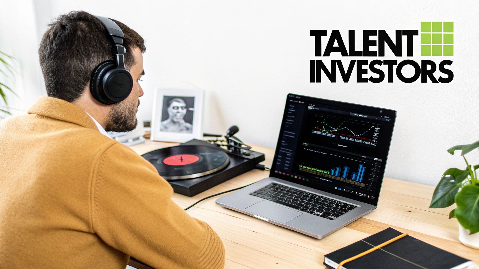 A man in headphones sits at a desk with a laptop displaying charts and a record player.