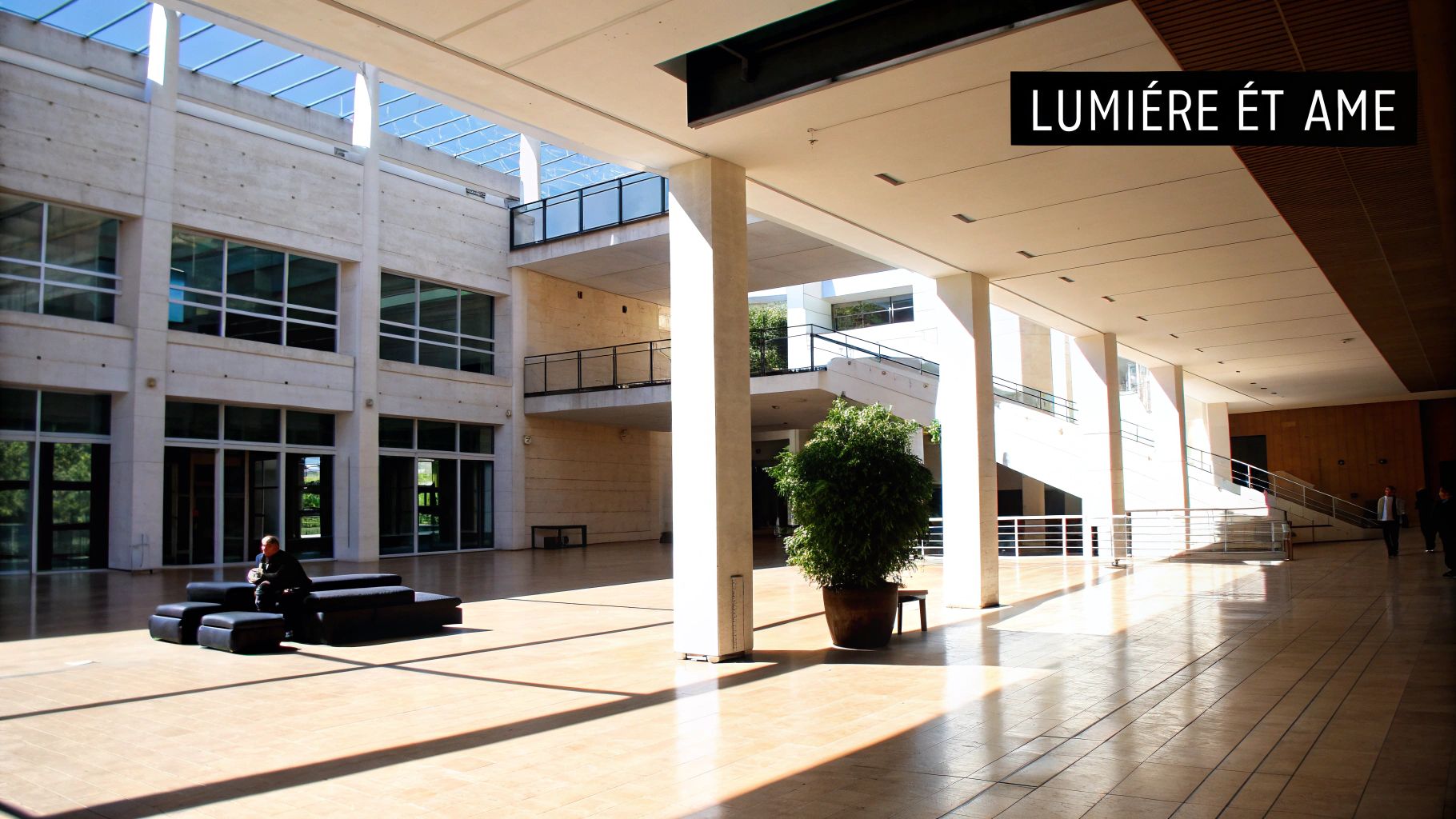 Un grand hall moderne et lumineux avec de hautes colonnes, des balcons et une personne assise, baigné de lumière naturelle.