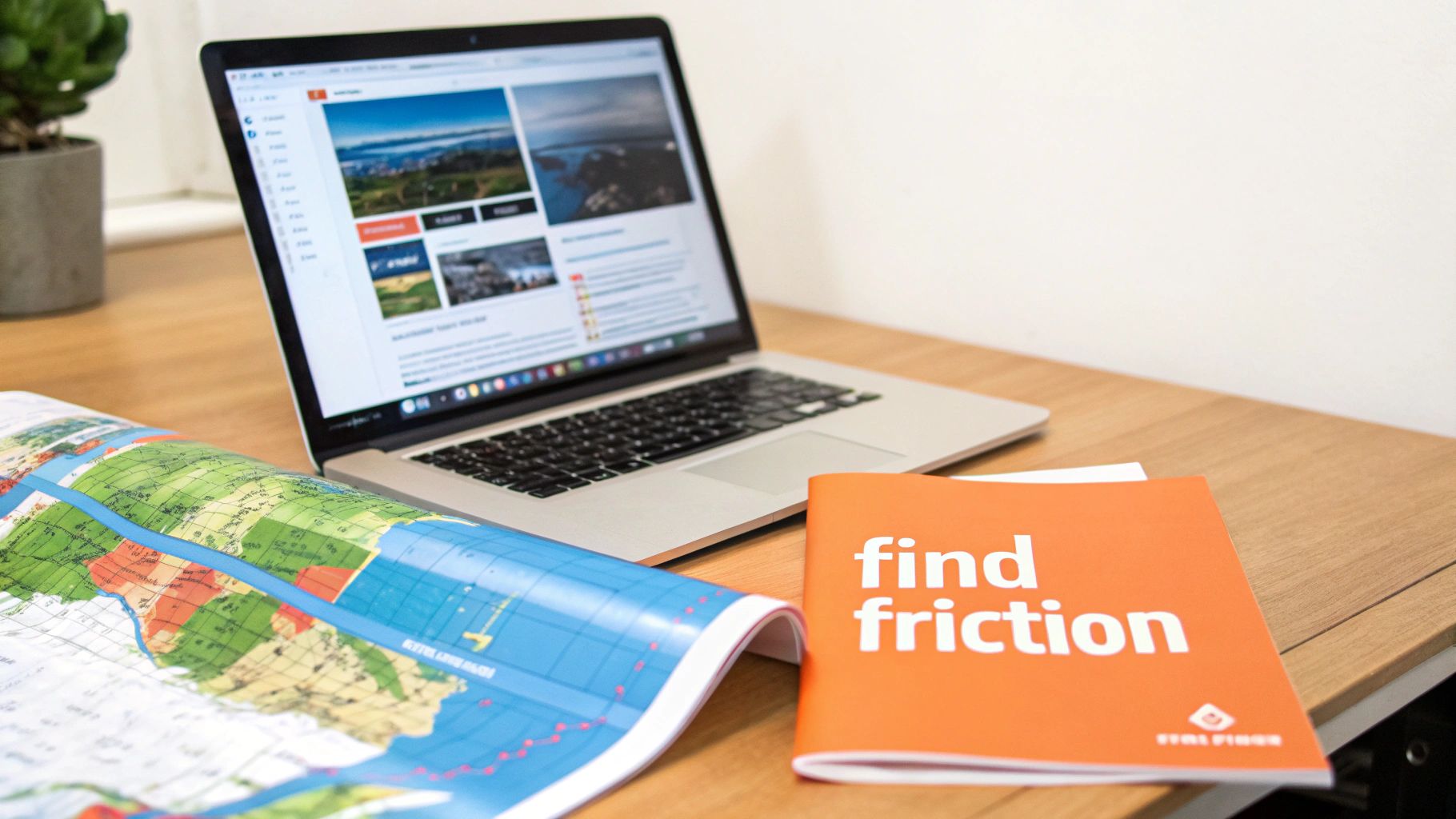 A laptop displaying a website, a world map, and an orange book on a wooden desk.