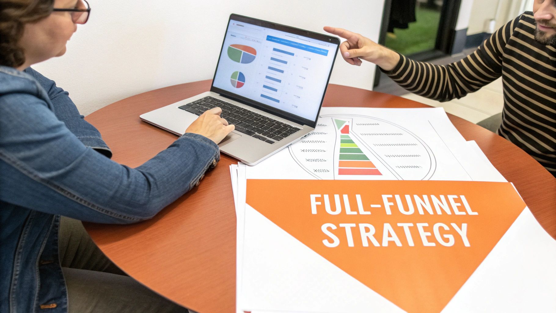Two people collaborating on a full-funnel strategy, reviewing data analytics on a laptop and documents.
