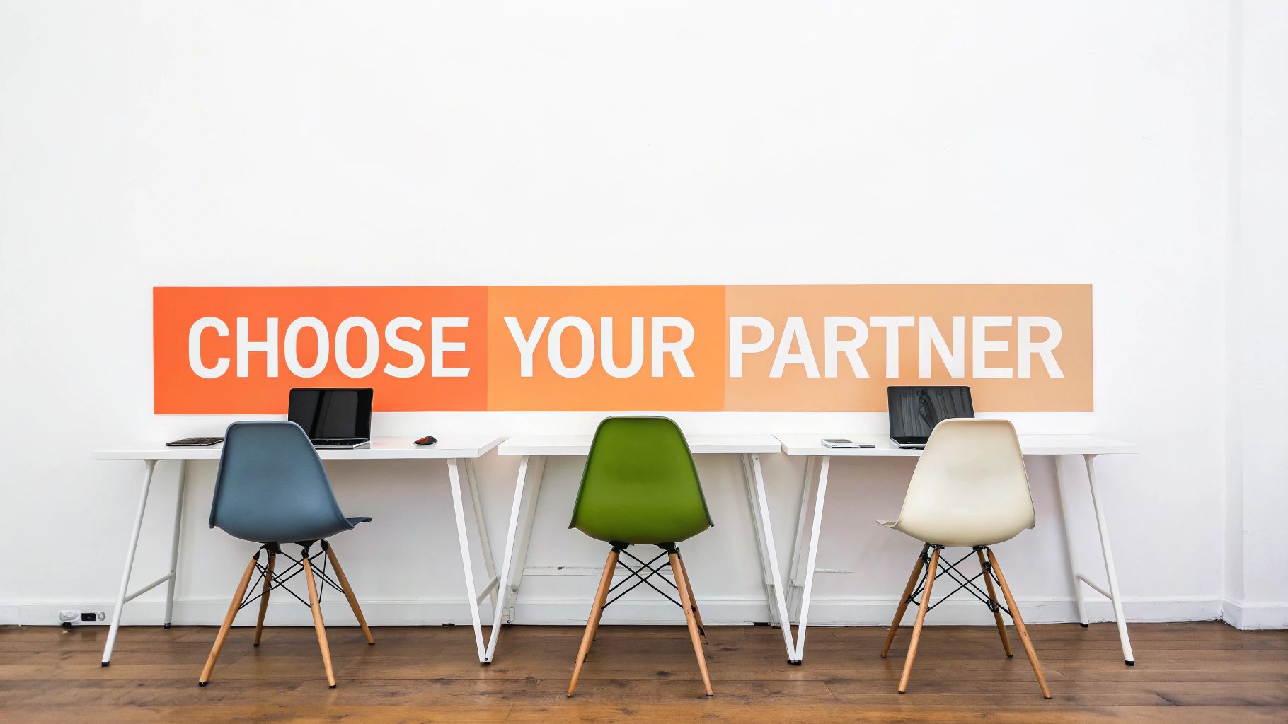 Three modern office workstations with colorful chairs and laptops, featuring a 'CHOOSE YOUR PARTNER' wall banner.