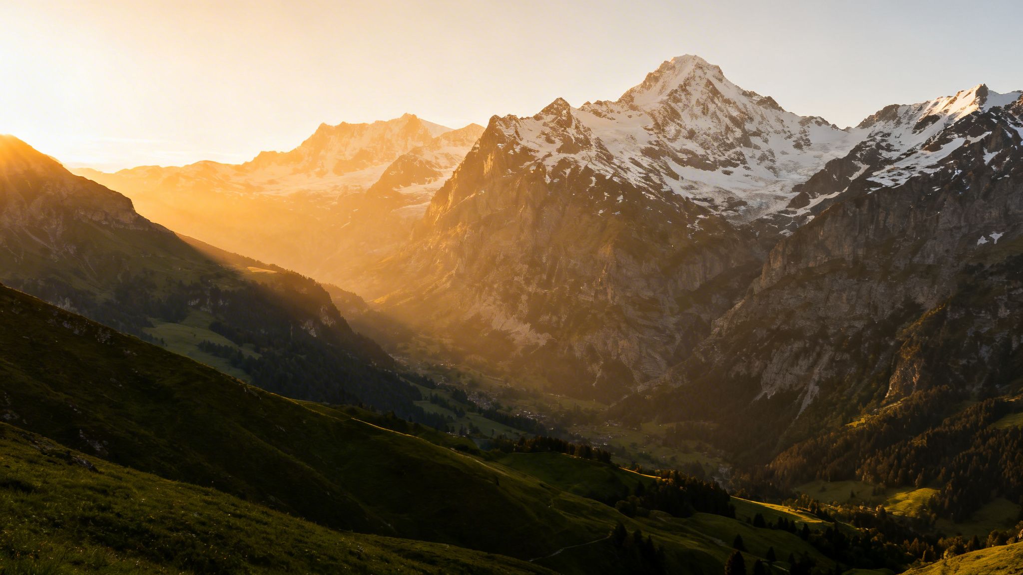 What is a greenway idea captured by golden sunset light over snow-capped peaks and green valleys in a mountain landscape.