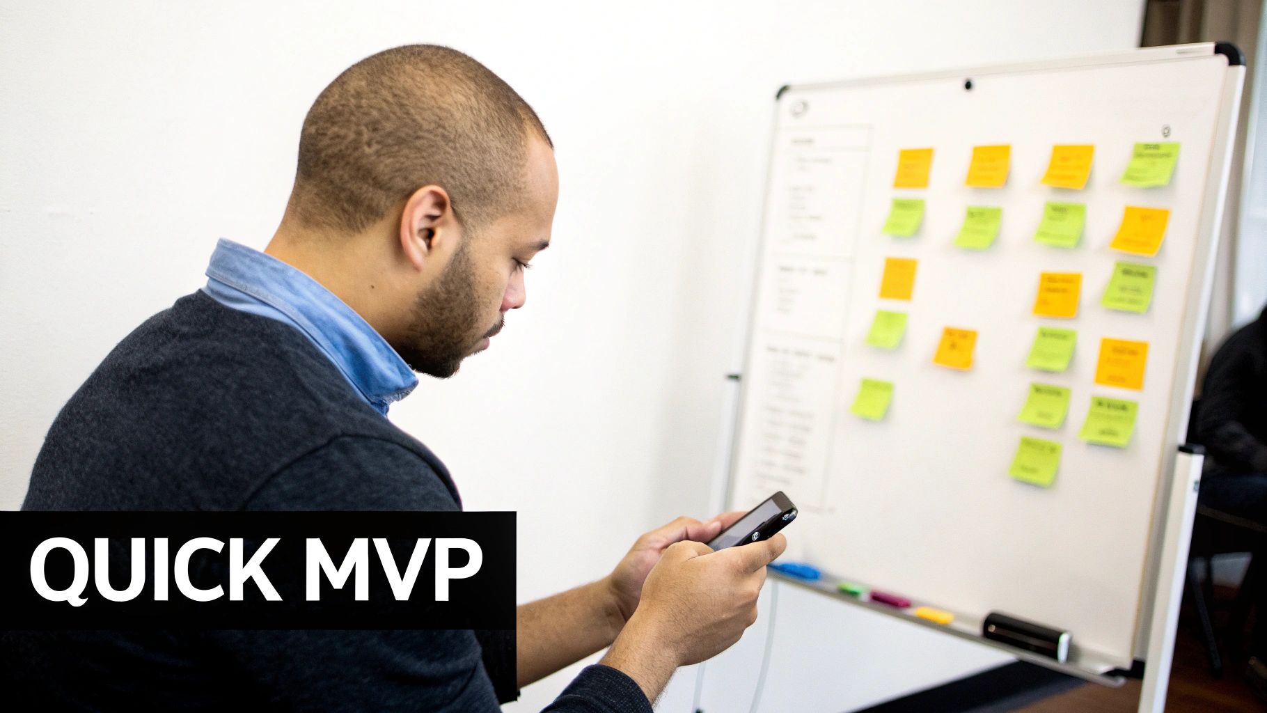 Side view of a man focused on his smartphone, next to a whiteboard with project sticky notes.