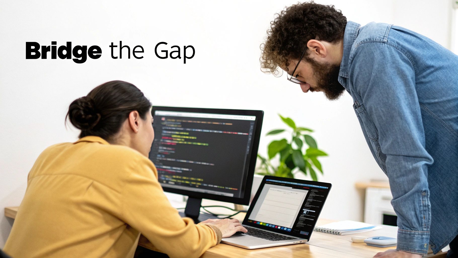 Two software engineers collaborate, reviewing code on dual computer screens in an office setting.