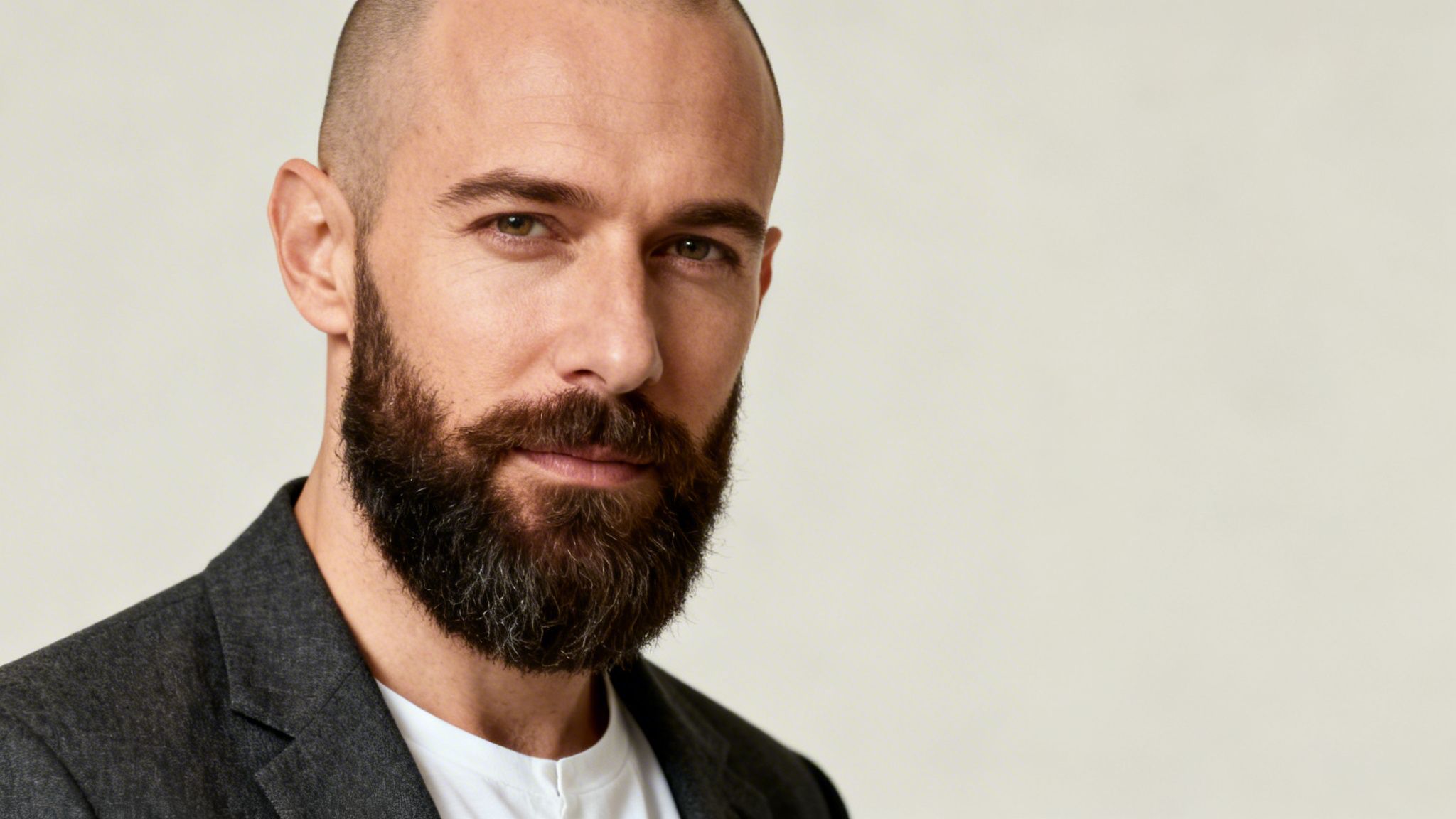 Nahaufnahme eines bärtigen Mannes mit Glatze und dunklem Sakko, der direkt in die Kamera blickt.