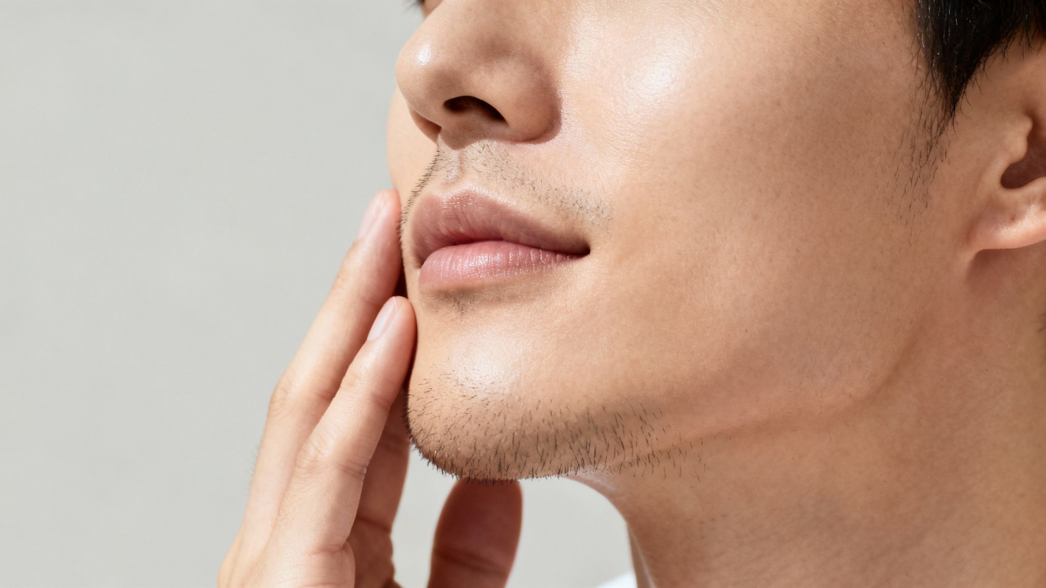 Nahaufnahme eines Mannes, der sein Gesicht berührt und kurze Bartstoppeln zeigt, mit gesunder Haut.