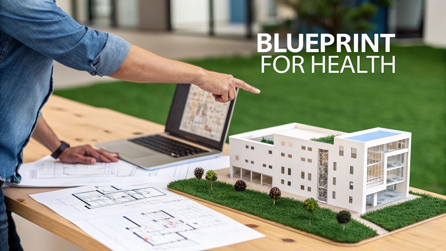An architect points at a modern hospital building model and blueprints on a wooden table.