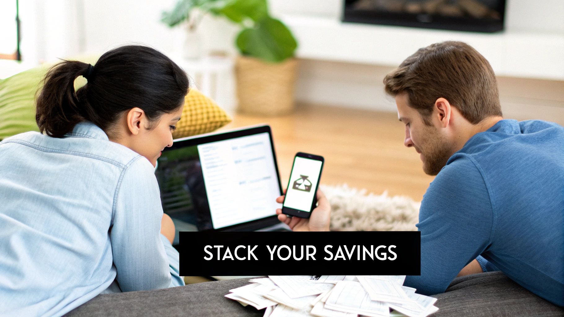 A couple, a woman and a man, lies on a couch, looking at a laptop and smartphone while budgeting.