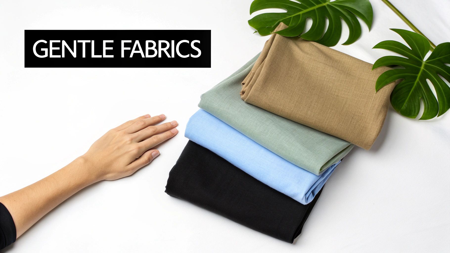 A stack of four different colored gentle fabrics next to a hand and tropical leaves.