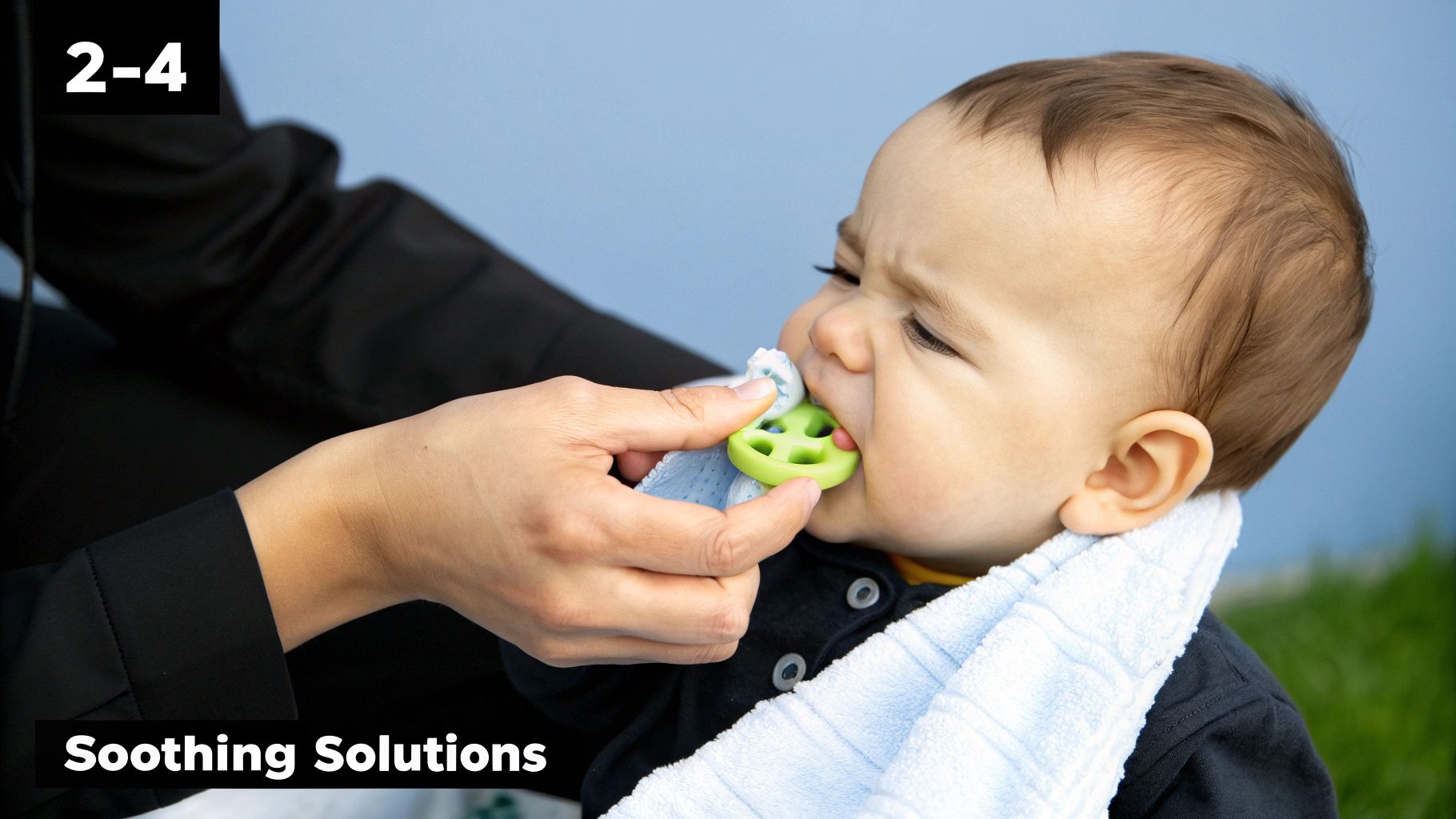 Close-up of an infant with a blue bib using a green teether for soothing relief, held by a parent.