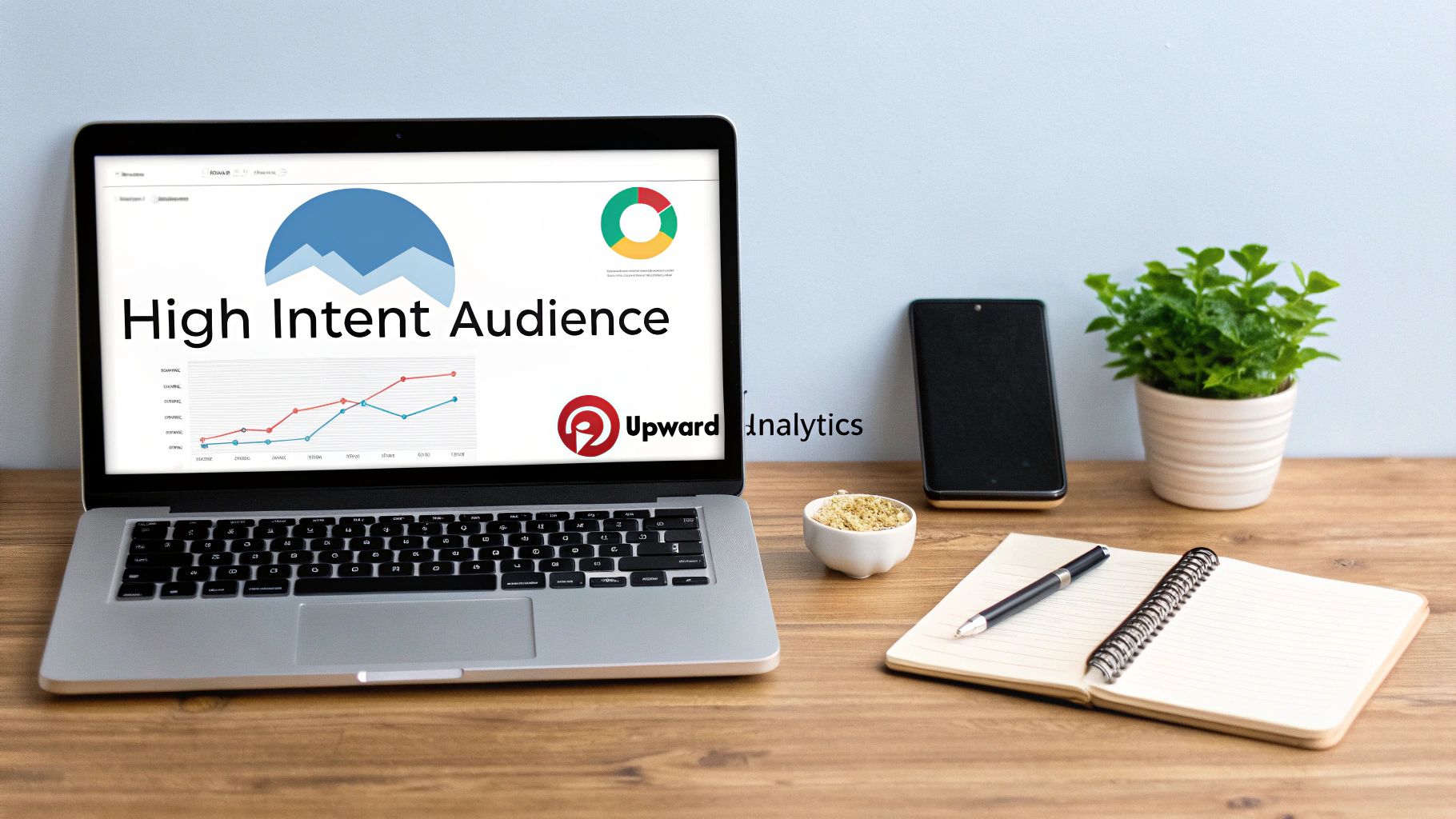 Workspace with laptop screen displaying high intent audience analytics from Pinterest using Upward Analytics, alongside growth charts, notebook, smartphone, and plant on wooden desk.