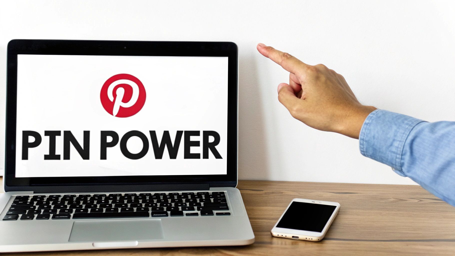 Person pointing at laptop screen displaying Pinterest logo and the words 'Pin Power' with a smartphone nearby on desk.