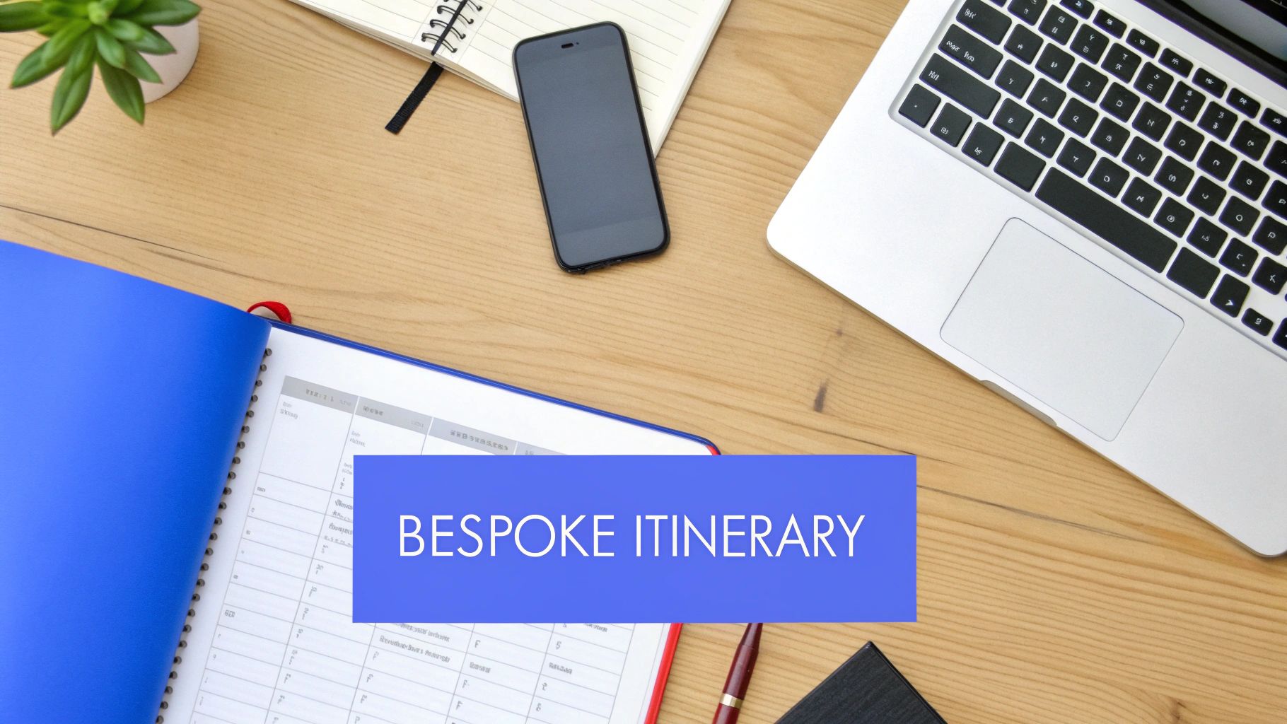 Overhead shot of a workspace with a laptop, phone, open blue binder, and a plant on a wooden desk. Text reads 'BESPOKE ITINERARY'.