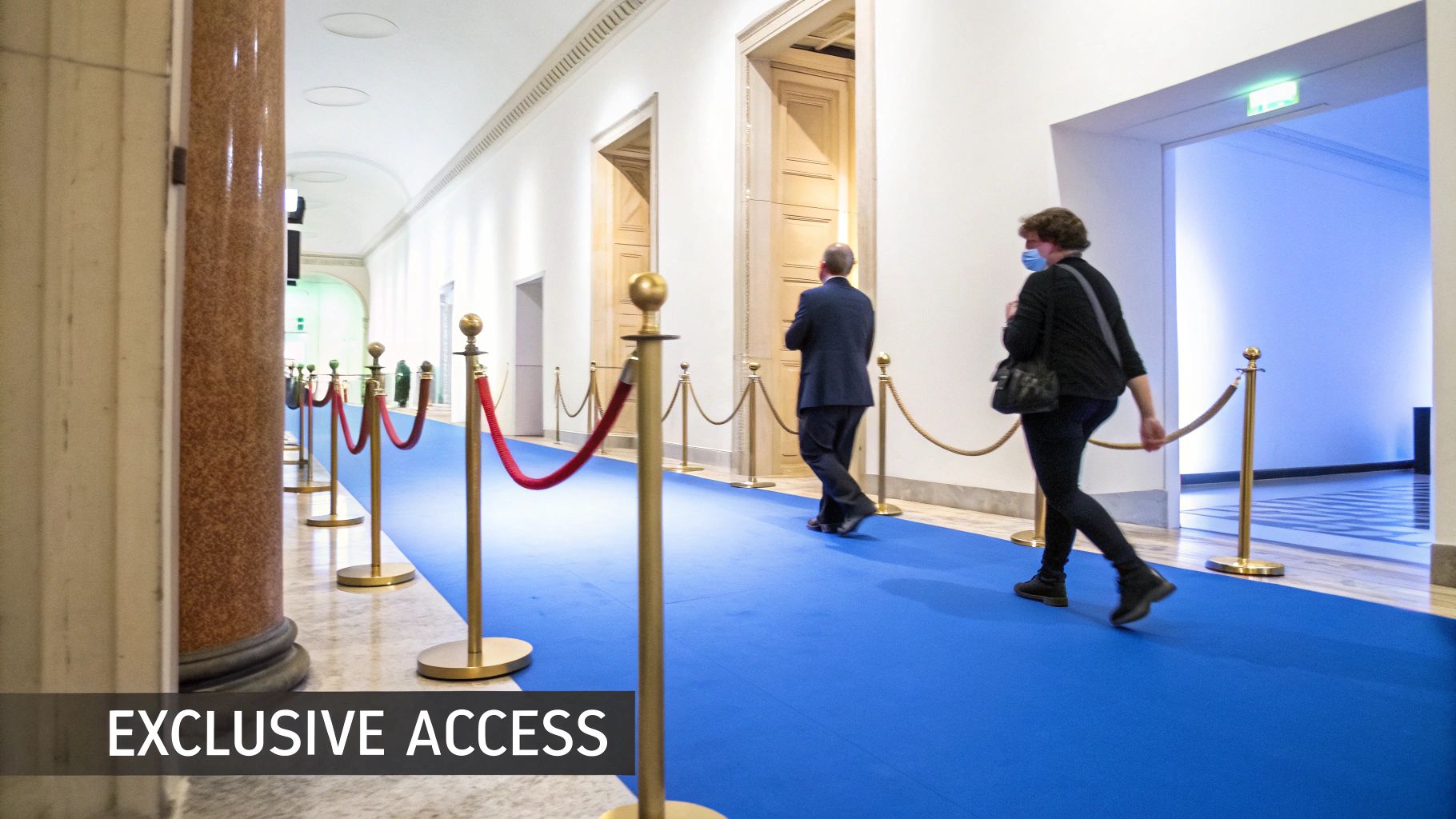 Elegant hallway with blue carpet, stanchions, and two individuals walking towards bright light.