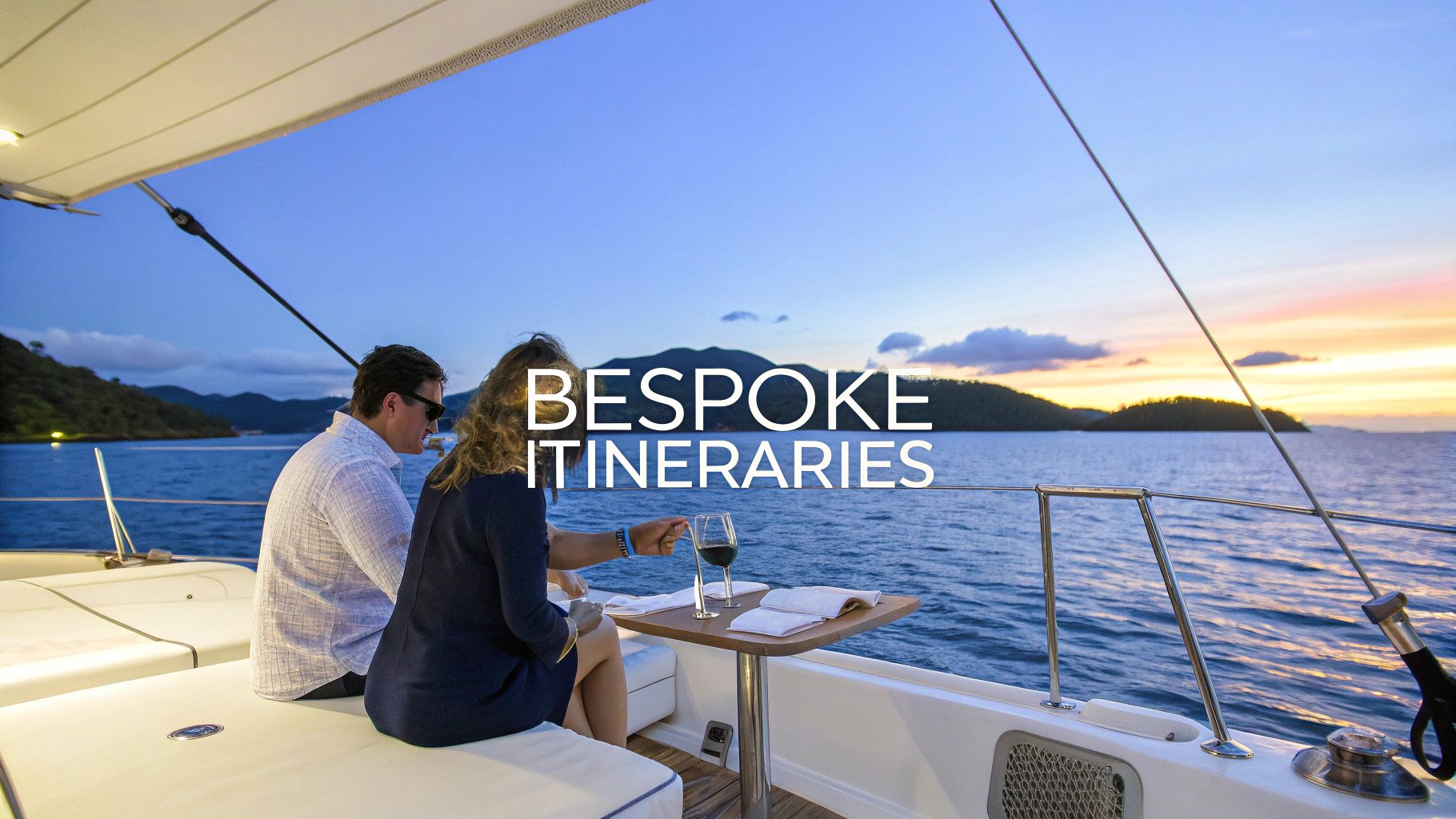 A private catamaran sails on the calm Aegean Sea near Santorini during a beautiful sunset.