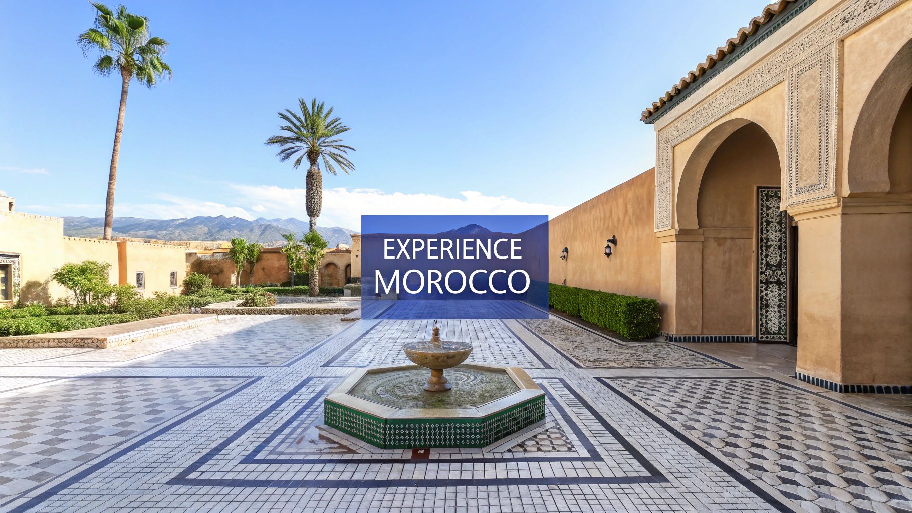 A beautiful Moroccan courtyard with a central fountain, palm trees, traditional architecture, and mountains under a blue sky.