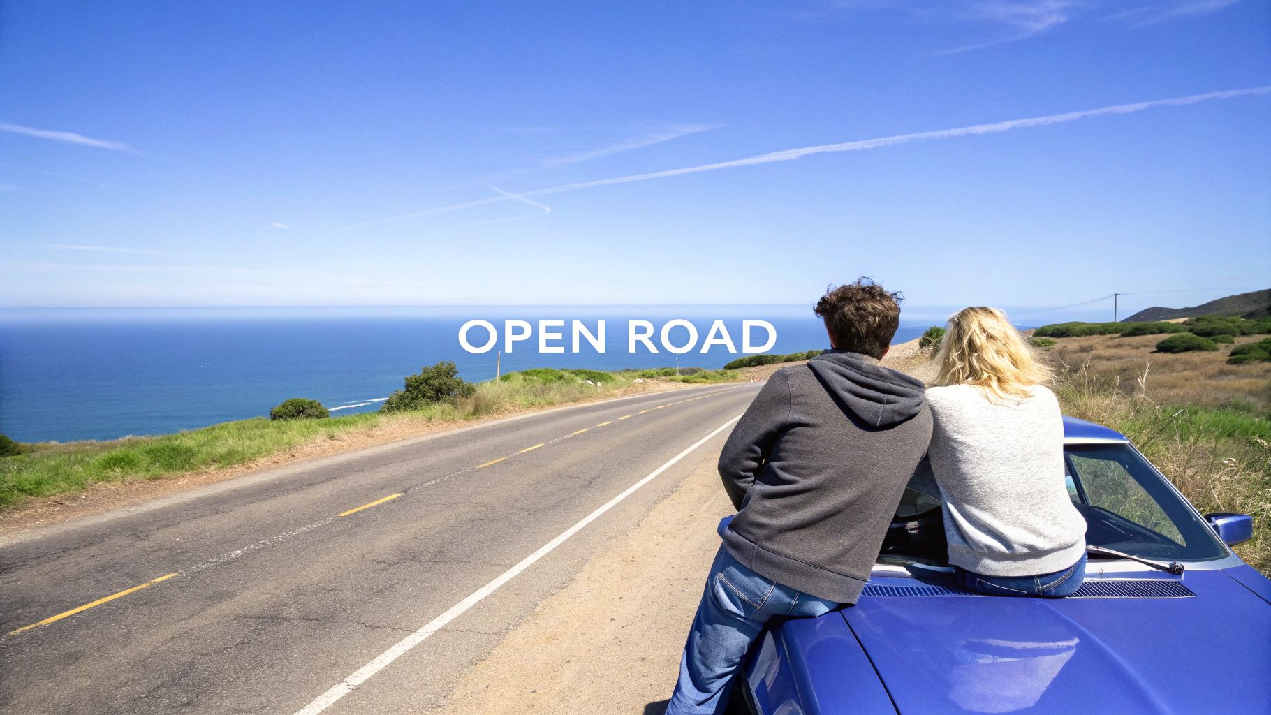 A couple sits on a blue car, admiring the scenic coastal road and vast ocean under a clear sky.