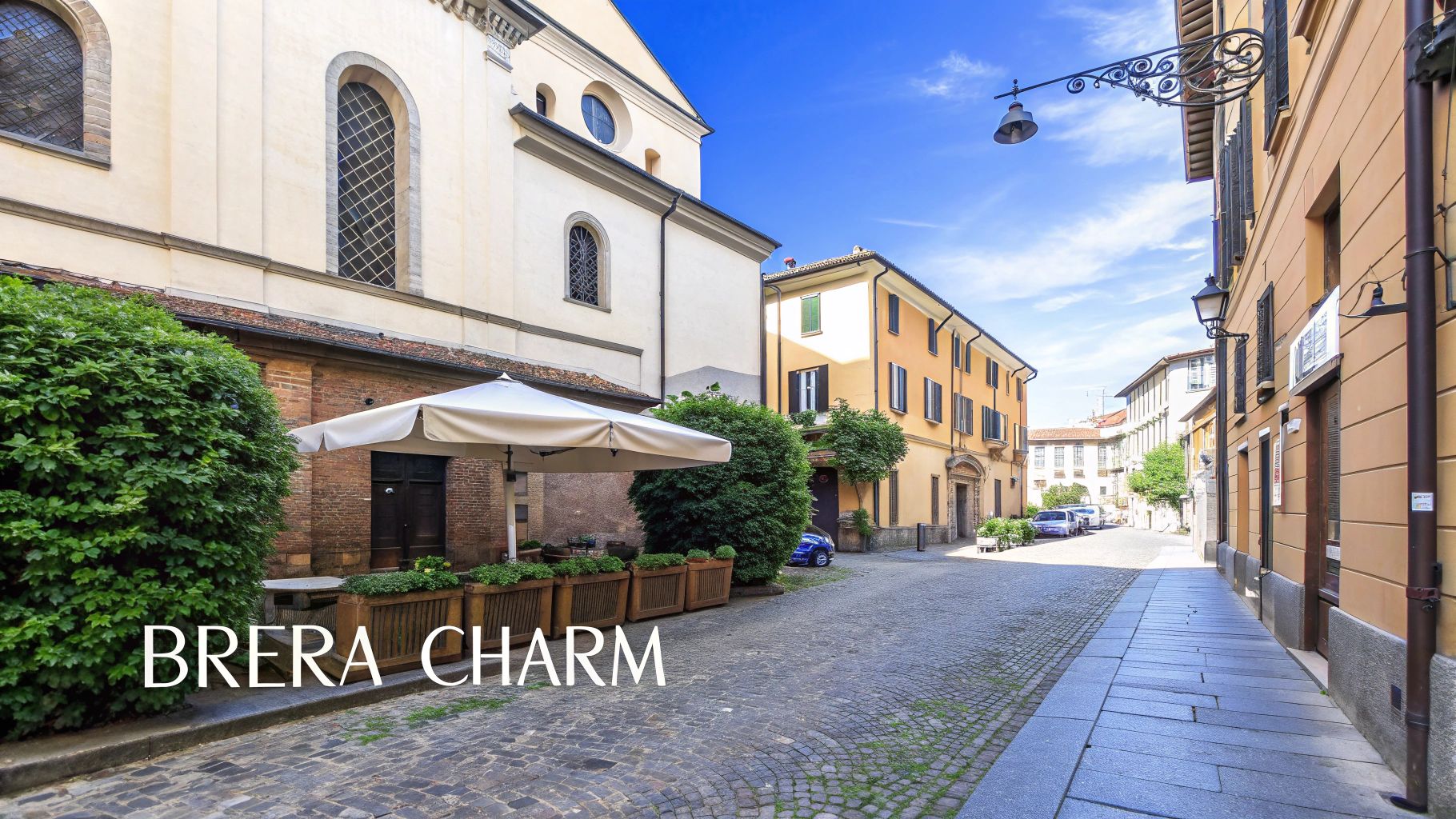 A picturesque cobblestone street in Brera, Milan, with historic buildings, a church, and an outdoor cafe area.