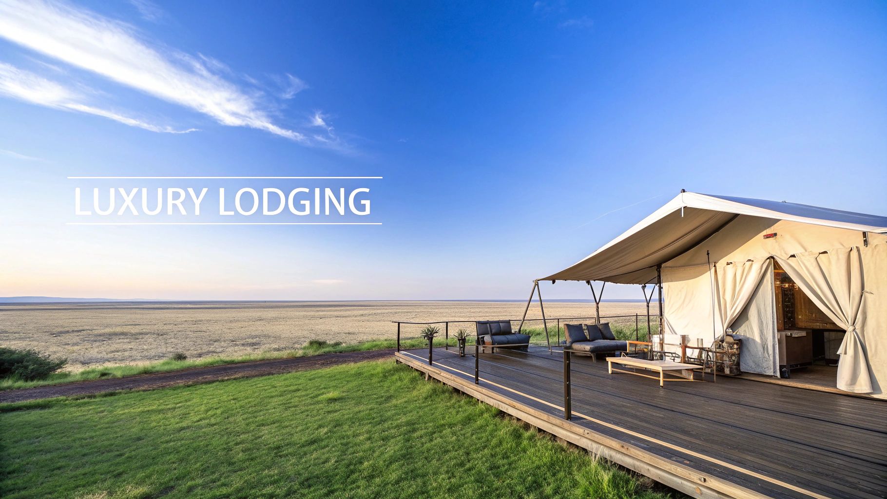 A luxury safari tent with a wooden deck and seating area, overlooking a wide, arid plain under a bright blue sky.