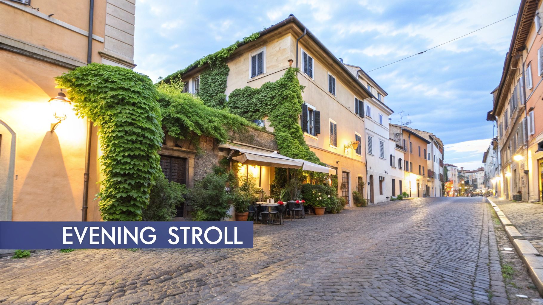 An illuminated cobblestone street with ivy-covered buildings and an outdoor cafe at twilight.