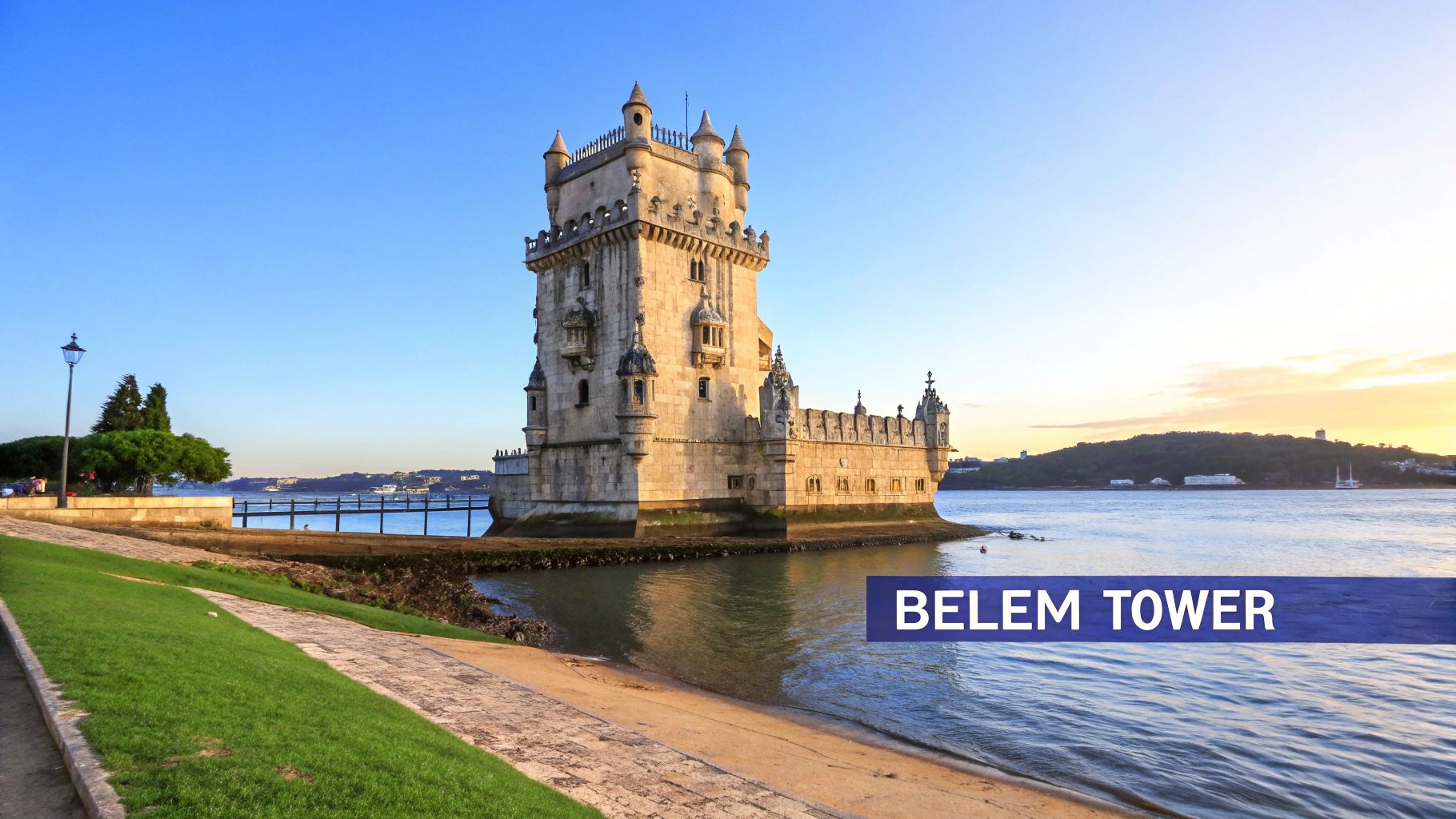 The historic Belem Tower in Lisbon, Portugal, stands majestically by the Tagus River at sunset, with a scenic path and green grass.