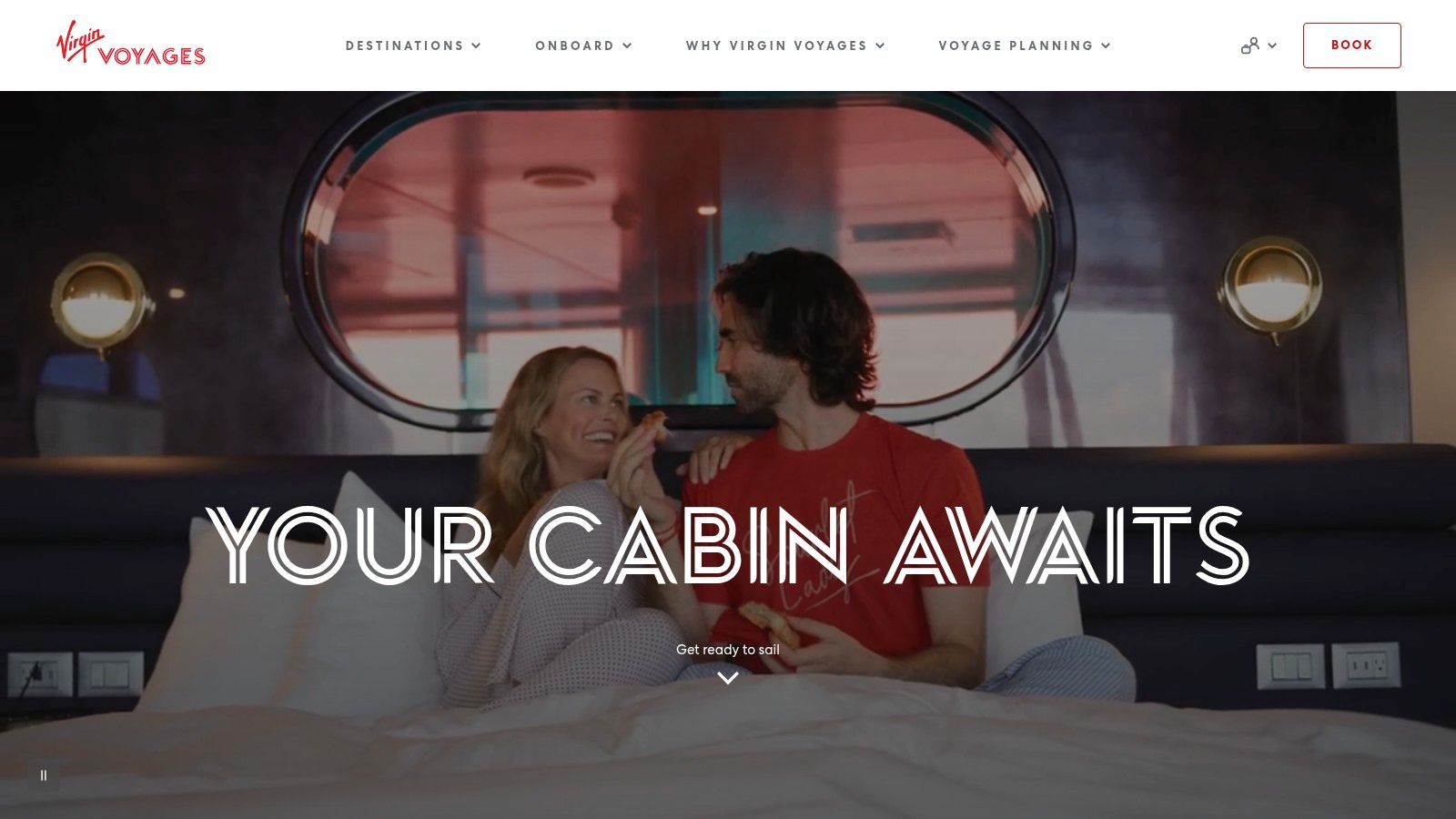 A modern, well-lit Virgin Voyages cabin with a large bed and a window view of the ocean.